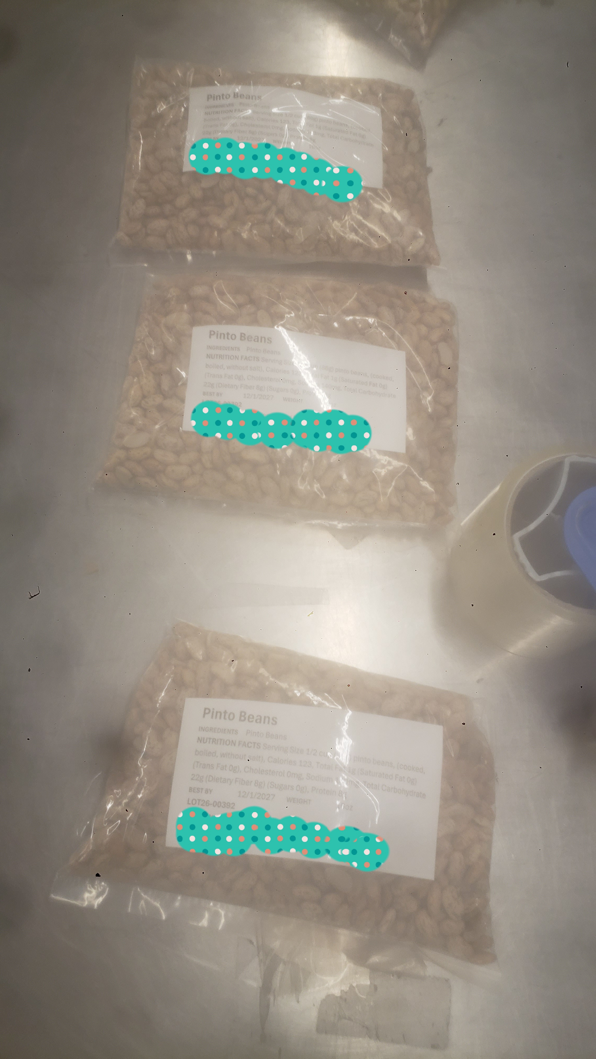 Three bags of pinto beans with label listing the name, nutrition facts, and other information on metal table.